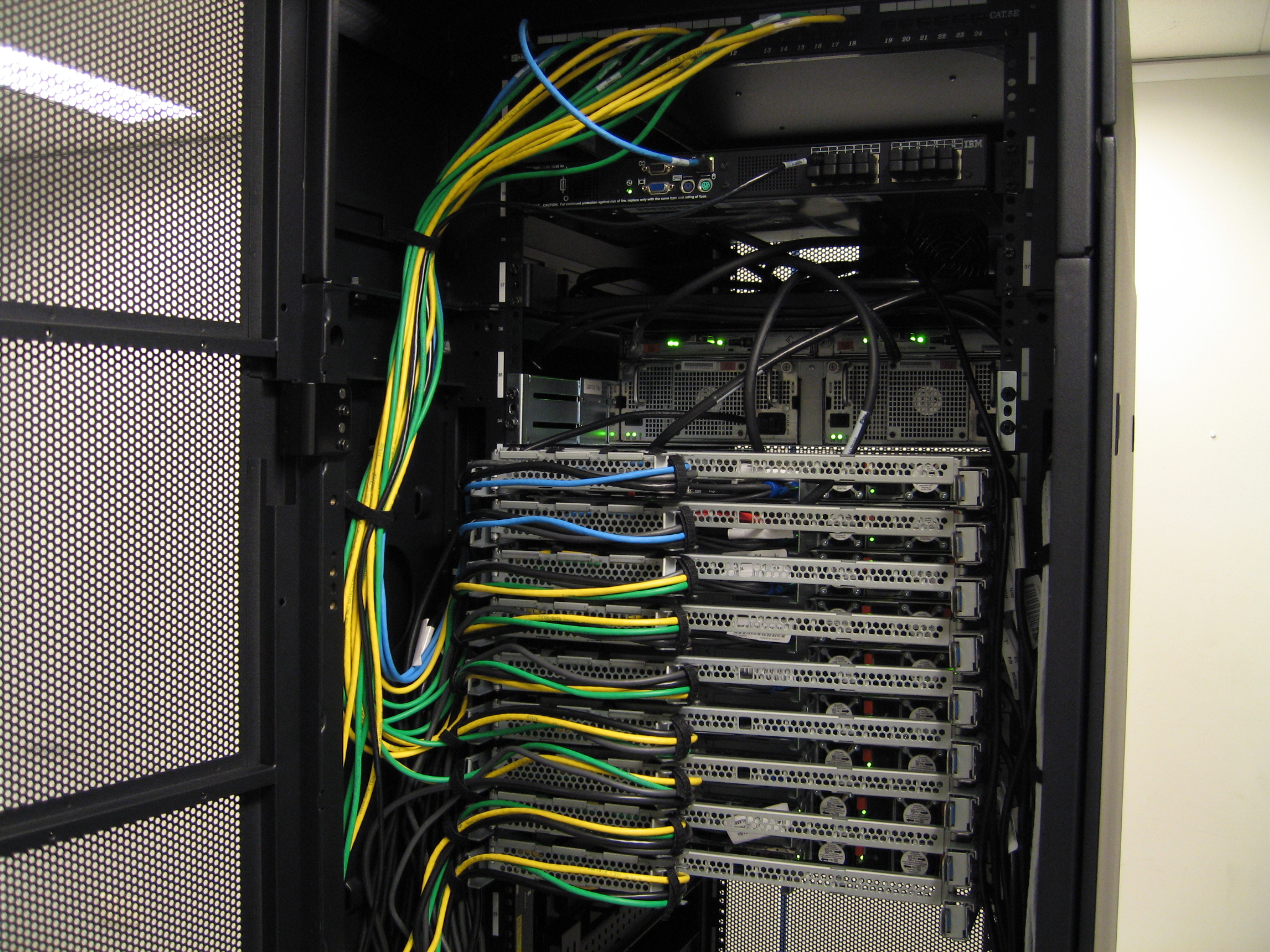 Baie informatique ouverte avec serveurs en rack reliés par des câbles réseau jaunes, verts, bleus et noirs.