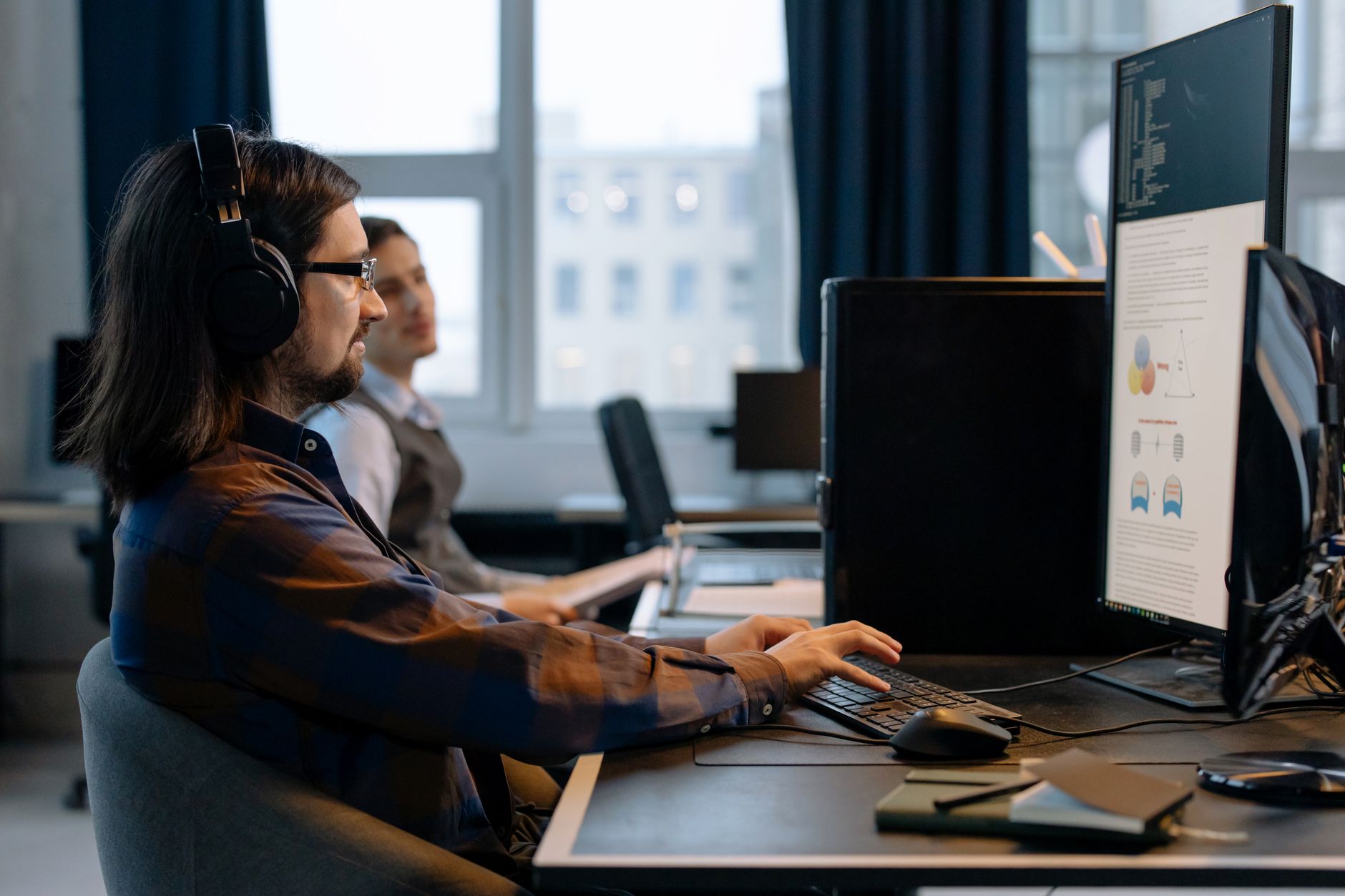 Un homme assis à un bureau avec un casque sur les oreilles regarde un écran d’ordinateur vertical.