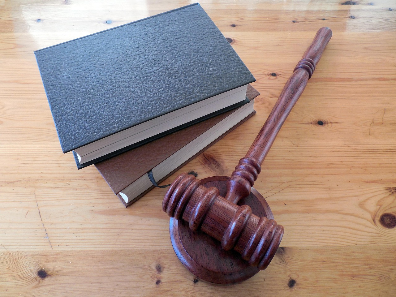 Un maillet de juge en bois posé sur son socle à côté de deux livres de droit empilés, sur une table en bois clair.
